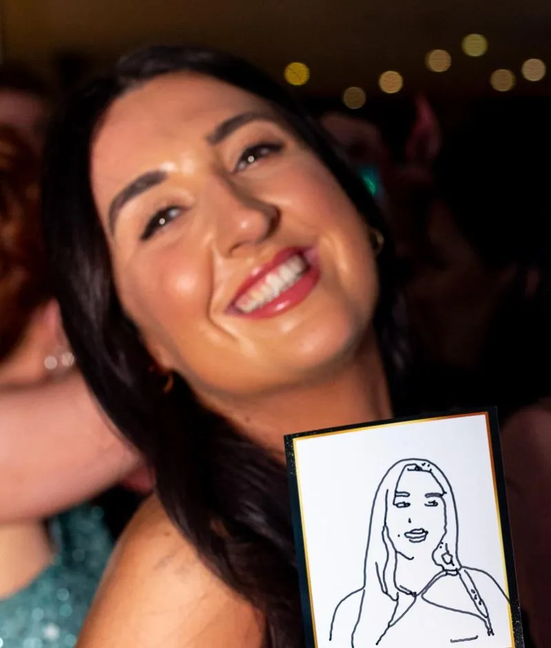 A smiling guest with her black-and-white ink portrait on a card