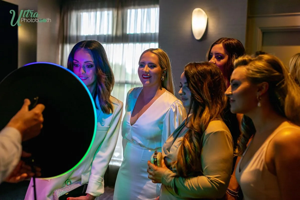 Guests smiling toward a handheld ring-light iPad booth at an indoor party