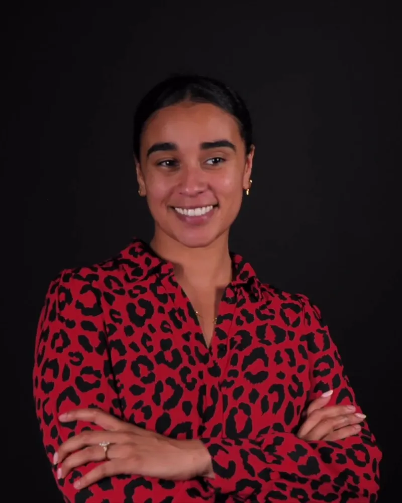 Smiling professional in a patterned blouse with crossed arms against a black backdrop