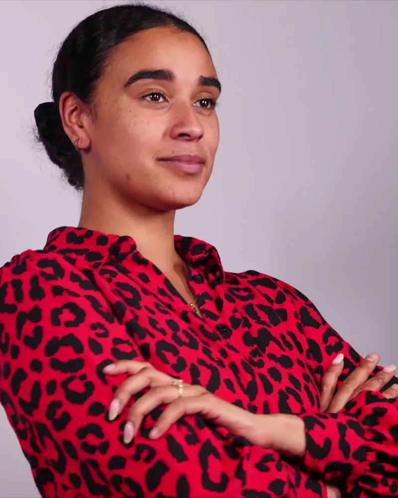 Professional in a patterned blouse posing with crossed arms against a gray backdrop