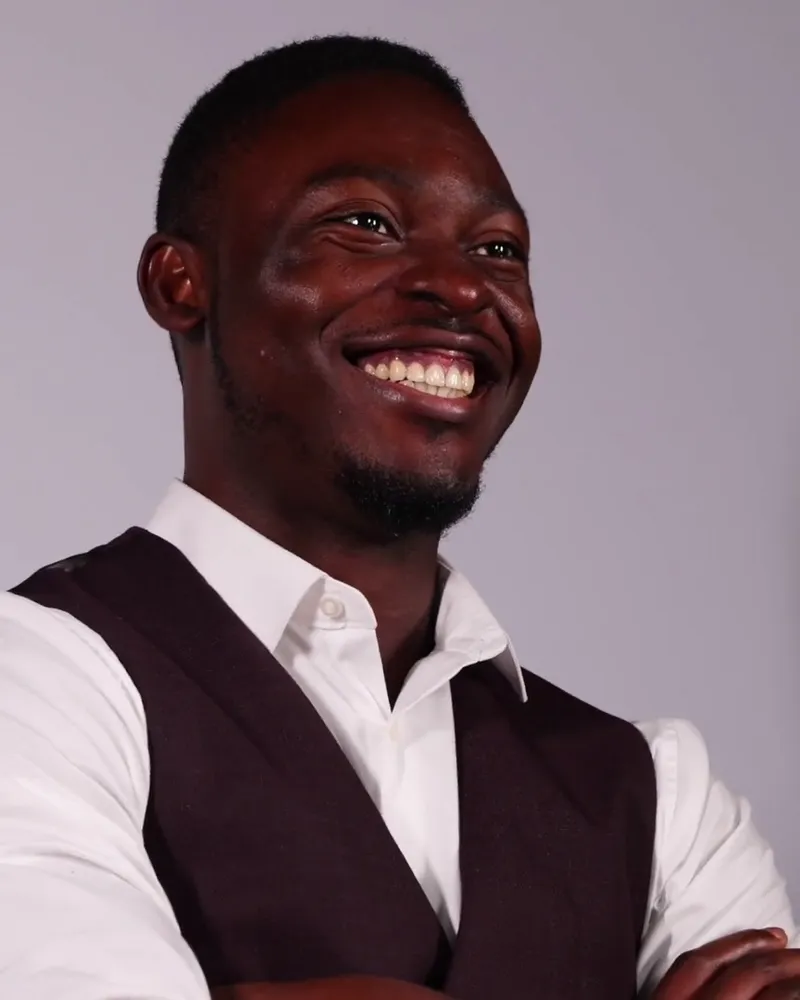 Smiling professional in a white shirt and dark vest against a gray backdrop
