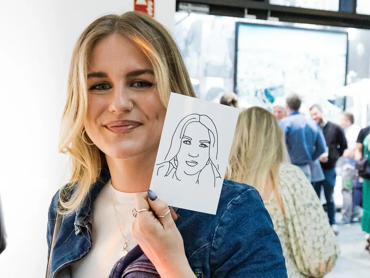 A smiling guest holding her finished robot-drawn ink portrait
