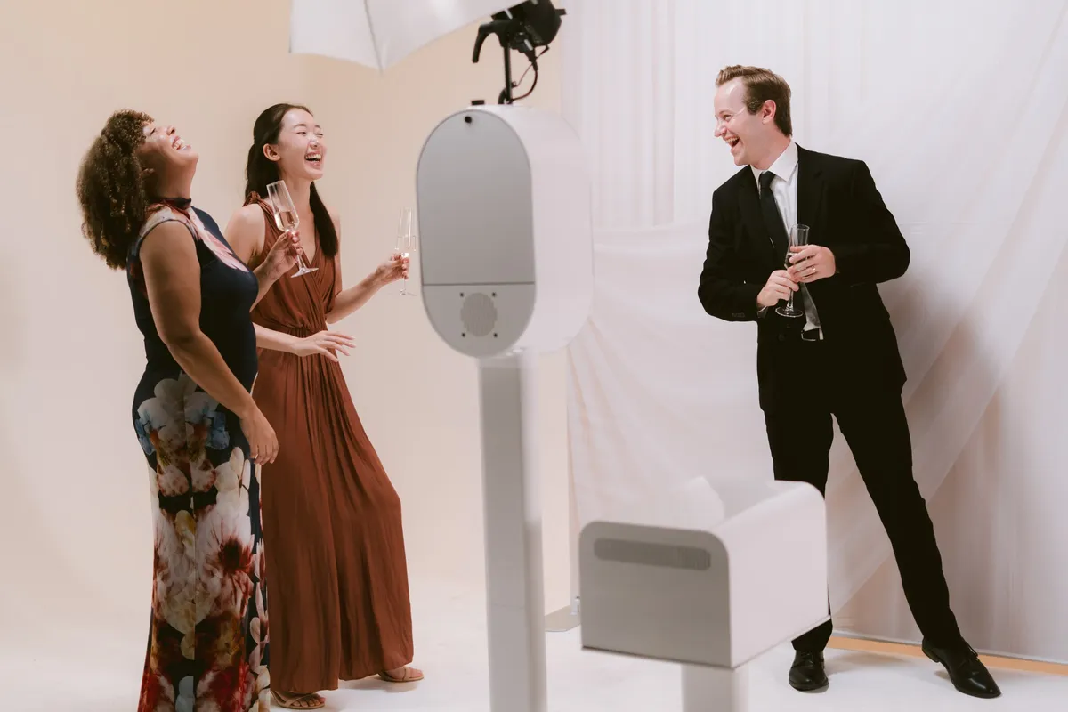 Guests laughing beside a white photo booth and printer