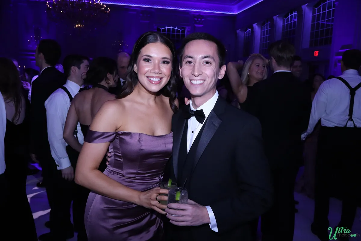 Two wedding guests smiling together in a purple-lit reception ballroom